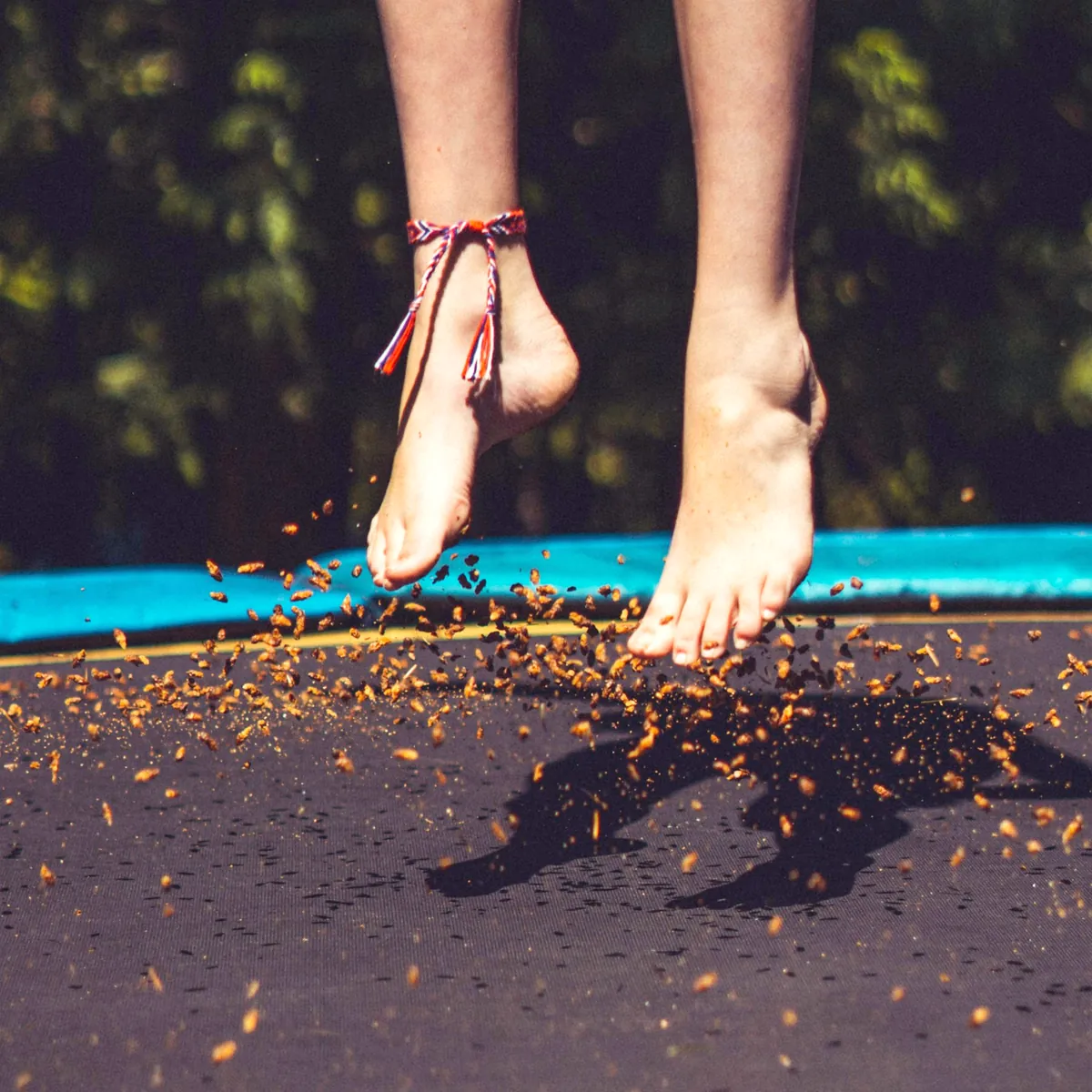 Trampolin üzerinde zıplayan çıplak ayaklar ve havaya savrulan yapraklar